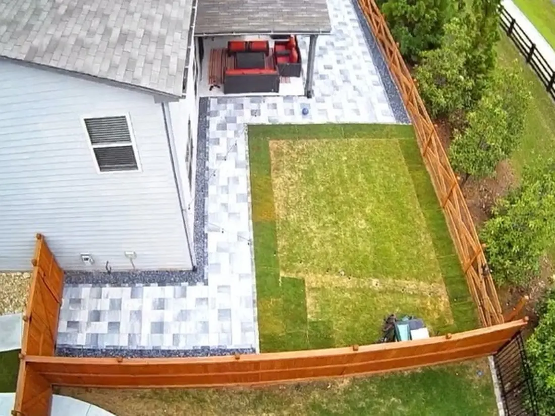 Aerial view of a wraparound paver patio with a covered pavilion and outdoor furniture behind a two-story home