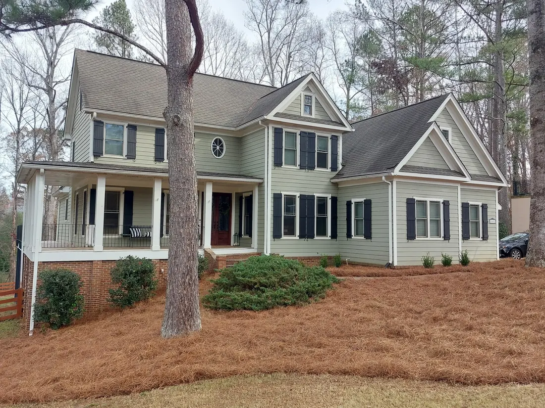 Front of a two-story home with wide beds freshly covered in pine straw