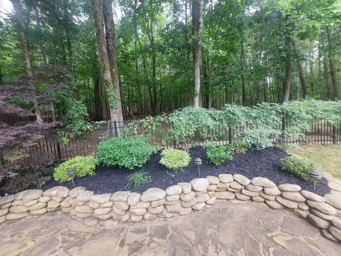 Stacked stone border edging a black mulch bed of new plantings at the tree line