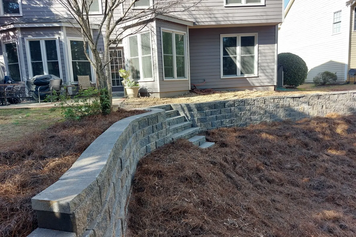 A curved block retaining wall with a finished cap holding back a pine straw bed